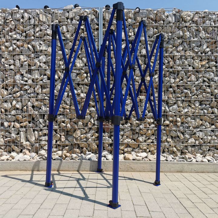 Hajotettu, mutta ei ammuttu sininen rakenne (kehys) saksettyjen juhlateltan, joka seisoo laatoituksessa kivien taustalla (aidan vieressä).